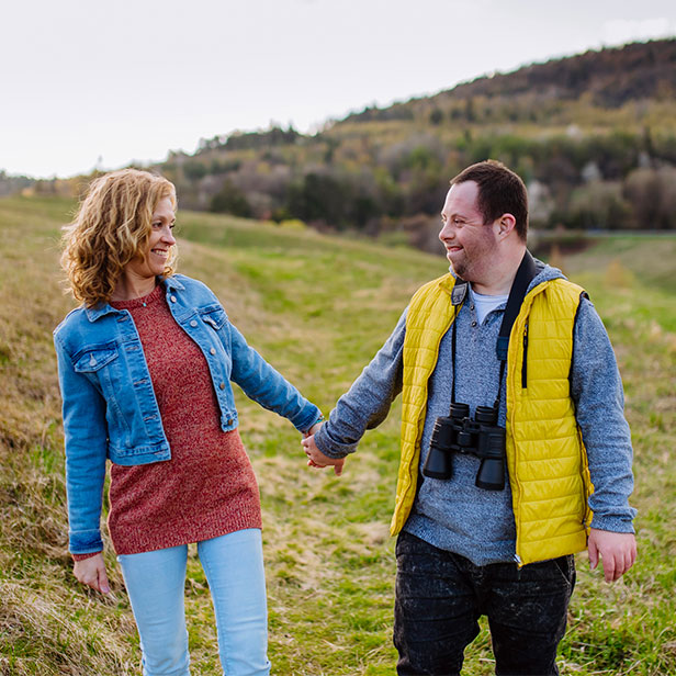 Happy young man with Down syndrome with his mother walking in nature, holding each other hands.