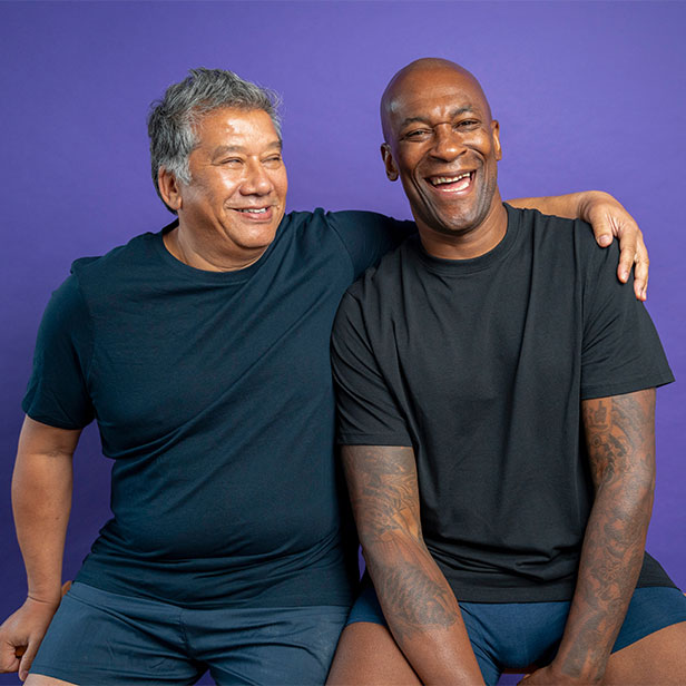 Portrait of two men laughing while sitting on bench against purple background