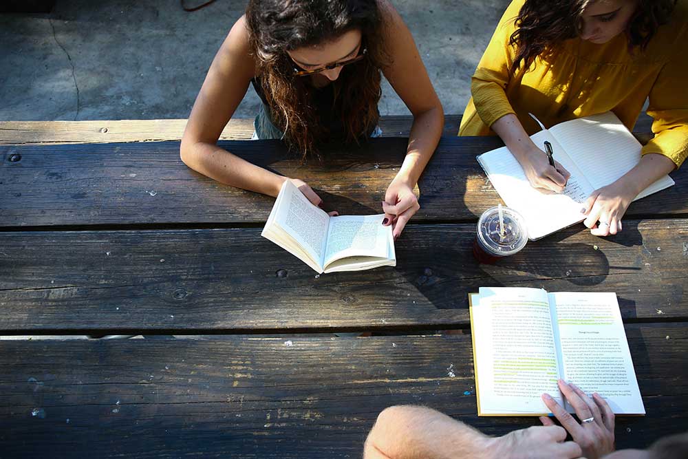 photograph for above of a table with three teenage girls reading and studying