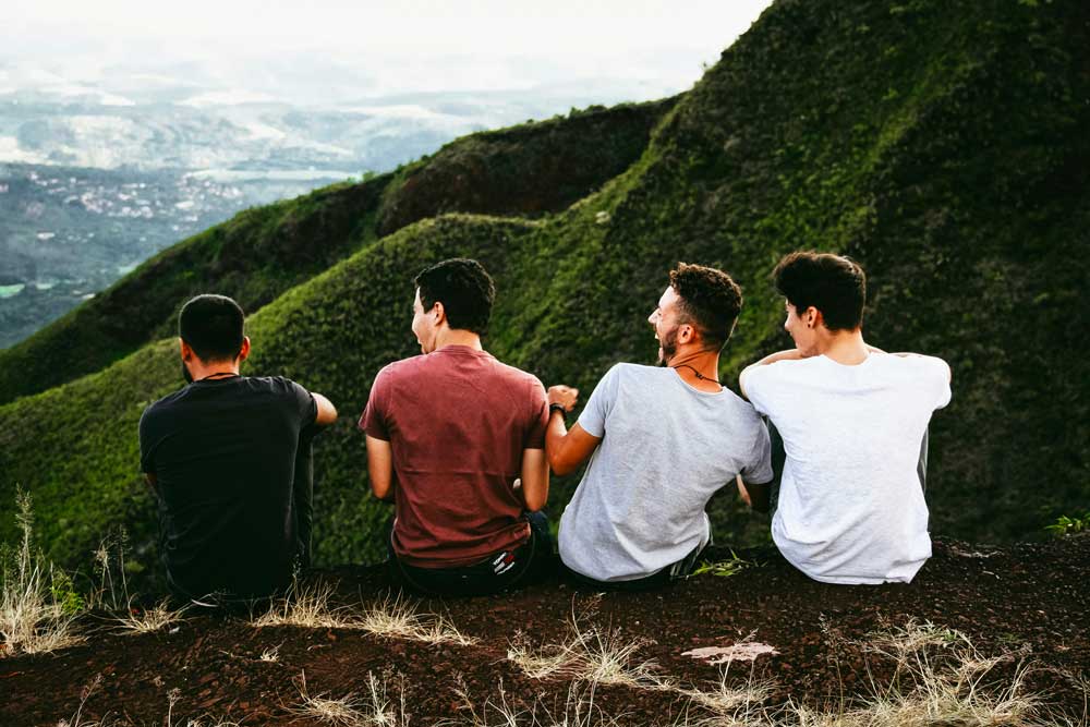 young men sitting on a rock atop of a mountian laughing
