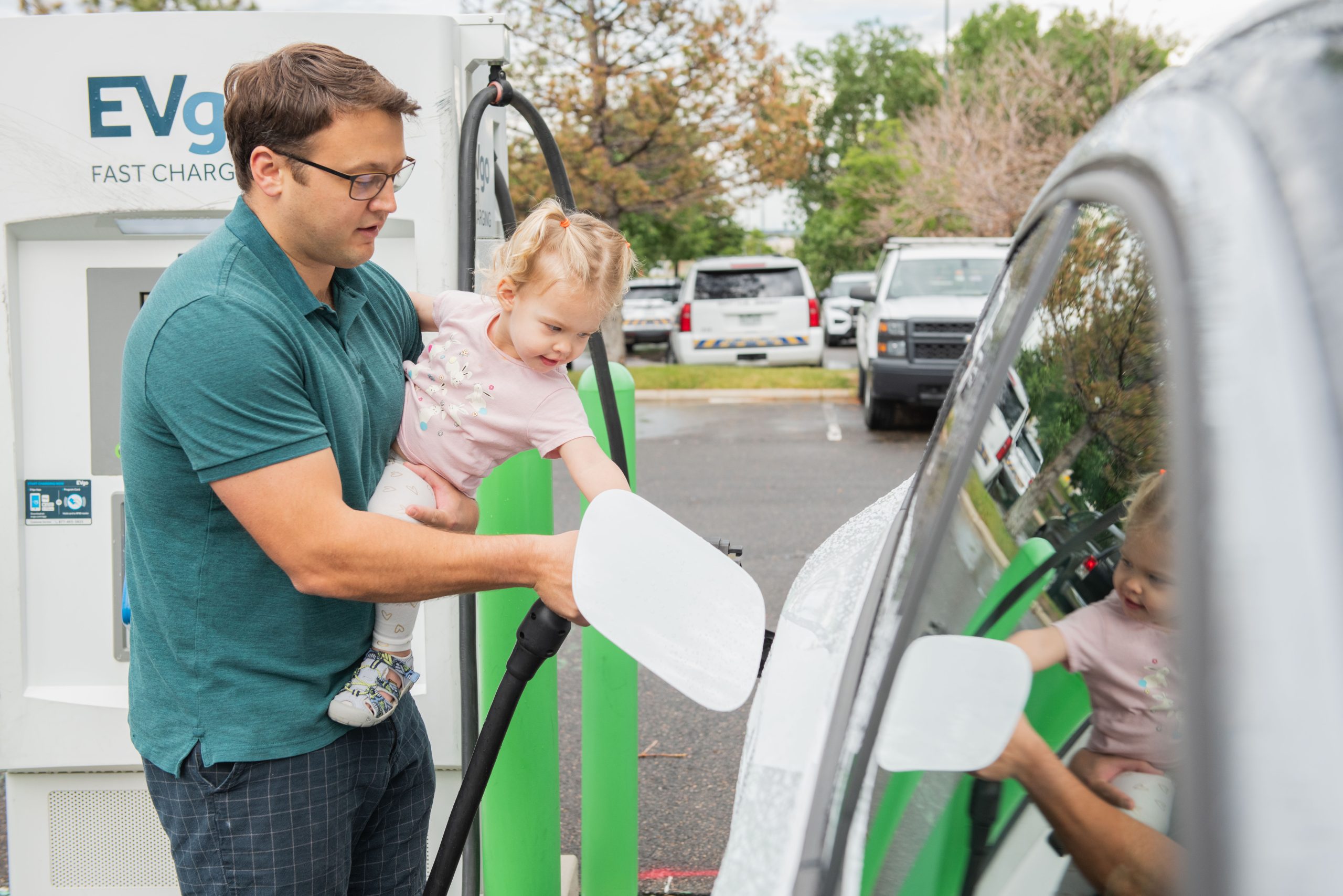 A Father and young daughter plug in an EV together at a public charging station