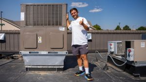 Parma-Heat-Pump A man stands next to a rooftop heat pump unit and gives thumbs up