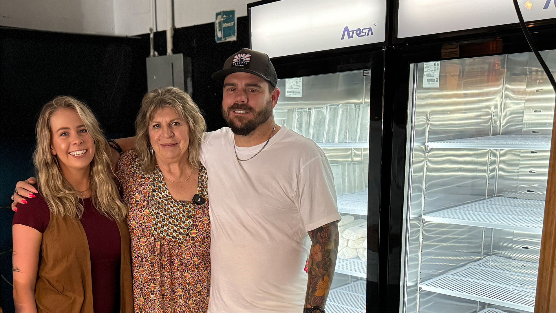 Henrys-Programs Three smiling business owners stand in front of their new, efficient refrigerator