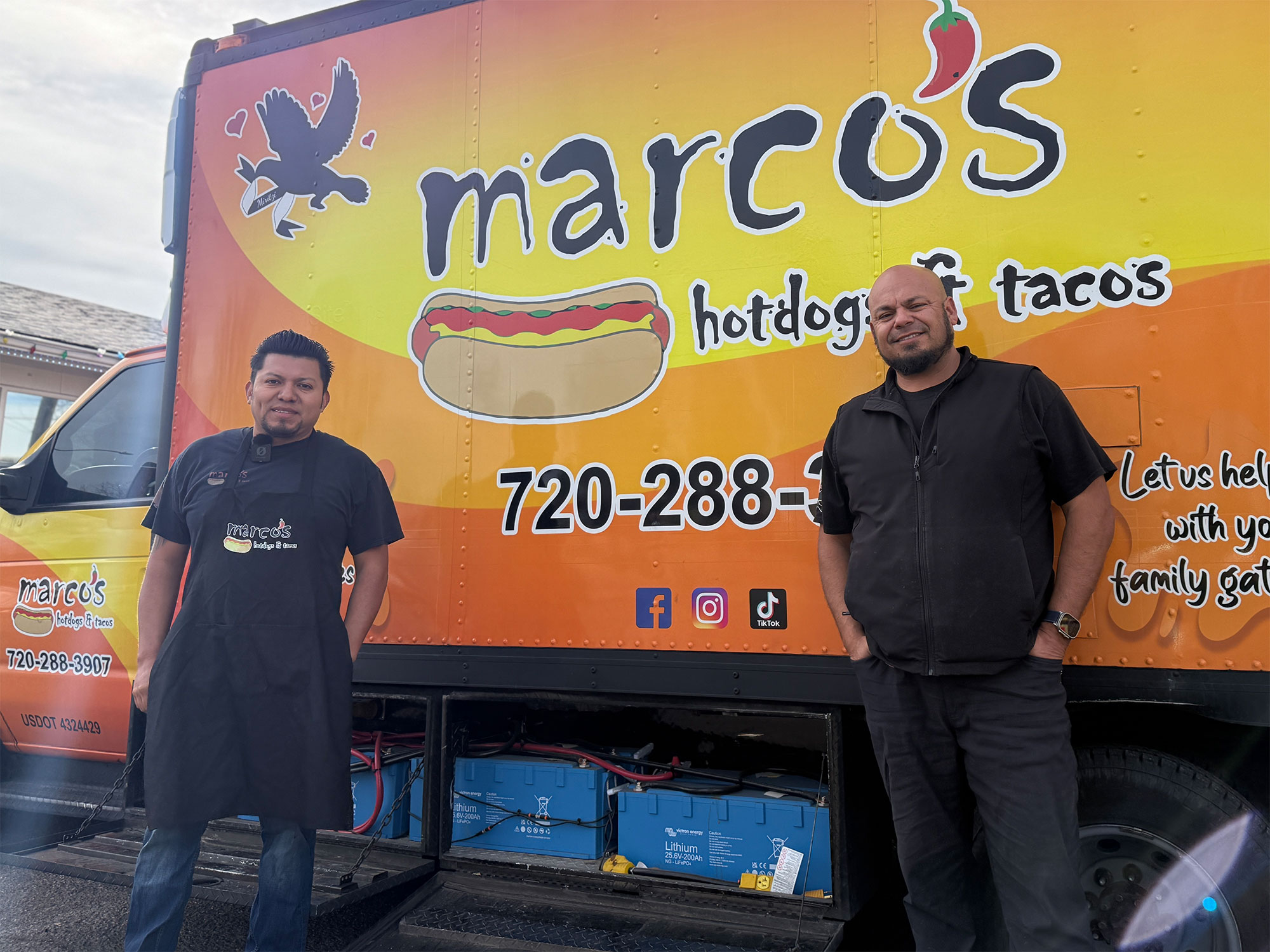 Two men stand in front of a food truck with the batteries shown in the bottom of the picture