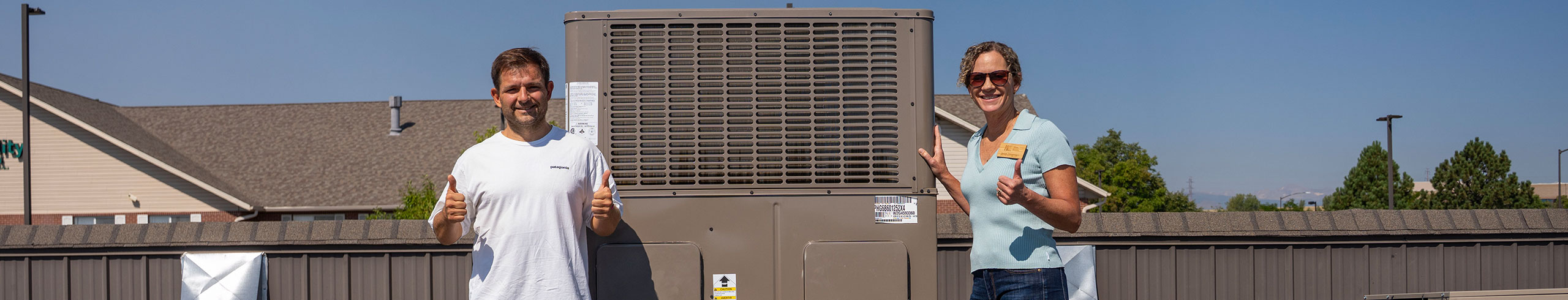 A man and a woman stand next to a hybrid rooftop HVAC system and give thumbs up