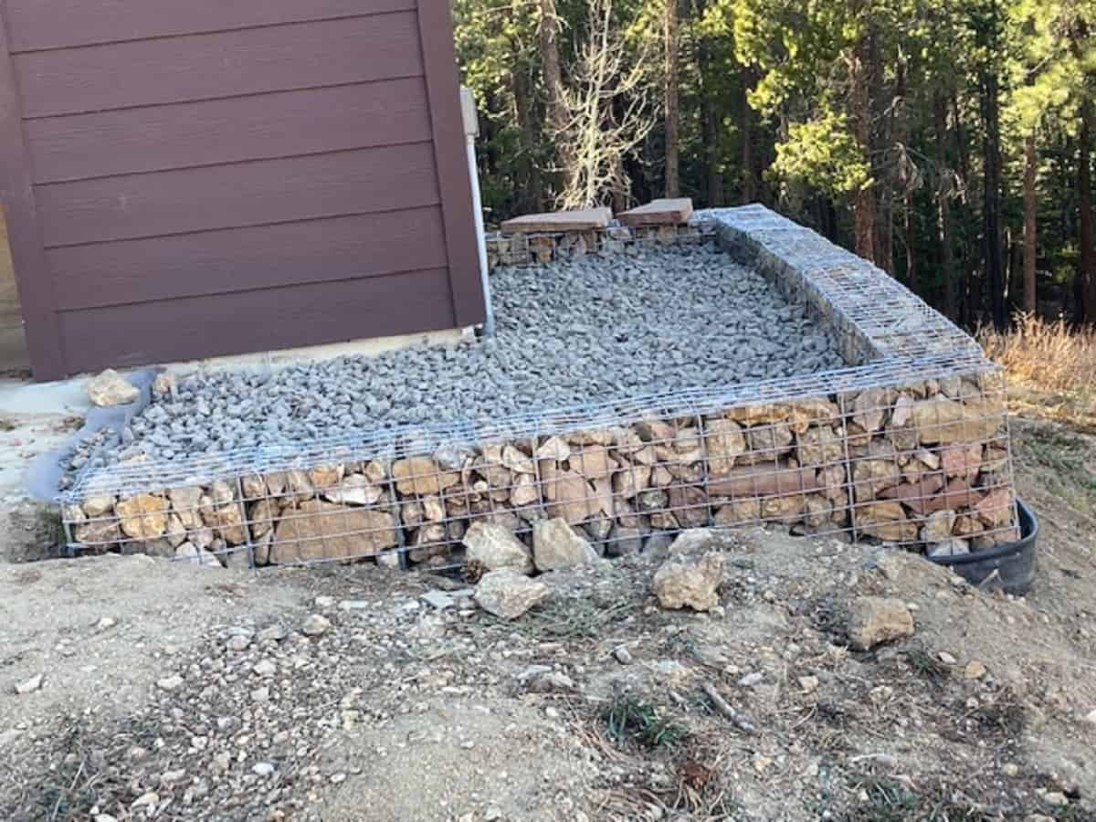 Coop wire filled with rocks forming terrace around corner of building