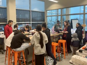 students at the library makerspace. Sitting at high table making things.